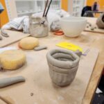 Group of students happily inspecting their fired pottery pieces fresh out of the kiln." "Close-up of a potter's hands skillfully coiling clay to form the base of a decorative vase